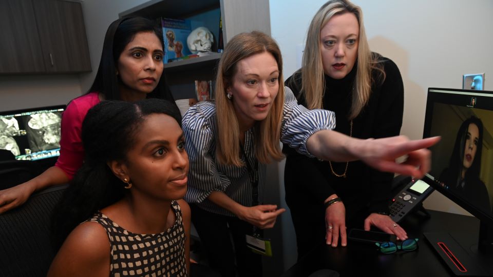 four people looking intently at an image on a computer screen