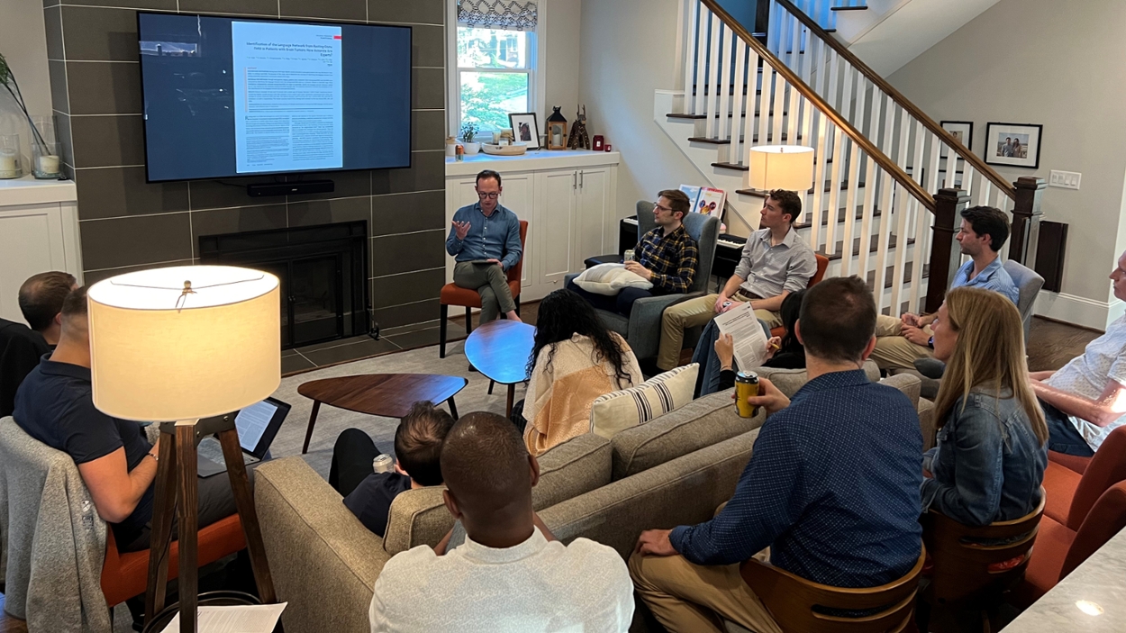 people sitting around a large living room reading from papers and a large screen on the wall