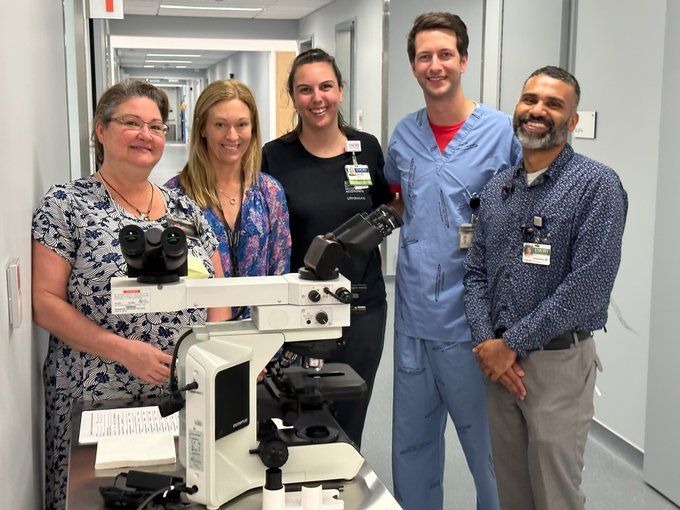 five people standing in the hallway of a hospital with a portable machine that is black and white