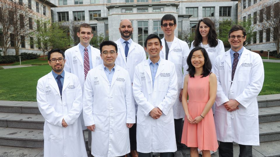 a group of people in white doctor coats standing in front of a marble building that says School of Medicine