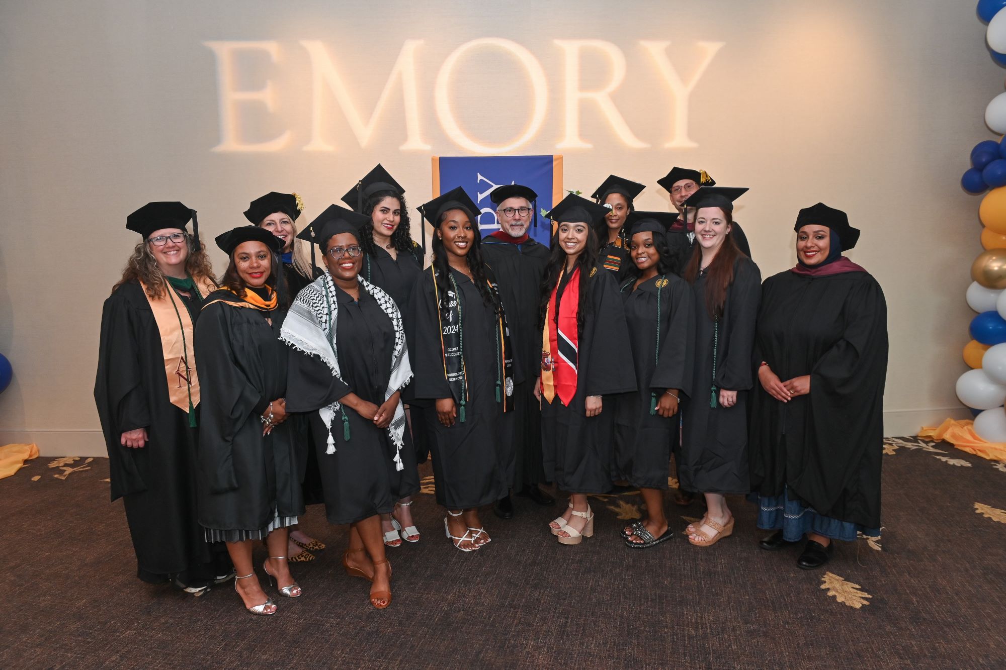 group of people wearing graduation caps and gowns in front of a lighted sign saying Emory