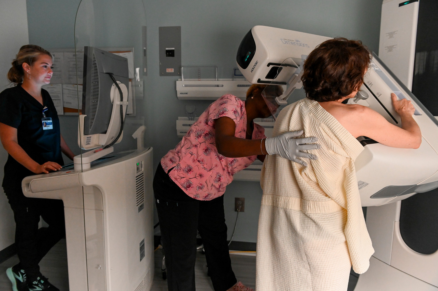 person positioning another position in mammography machine while another tech looks at images on screen