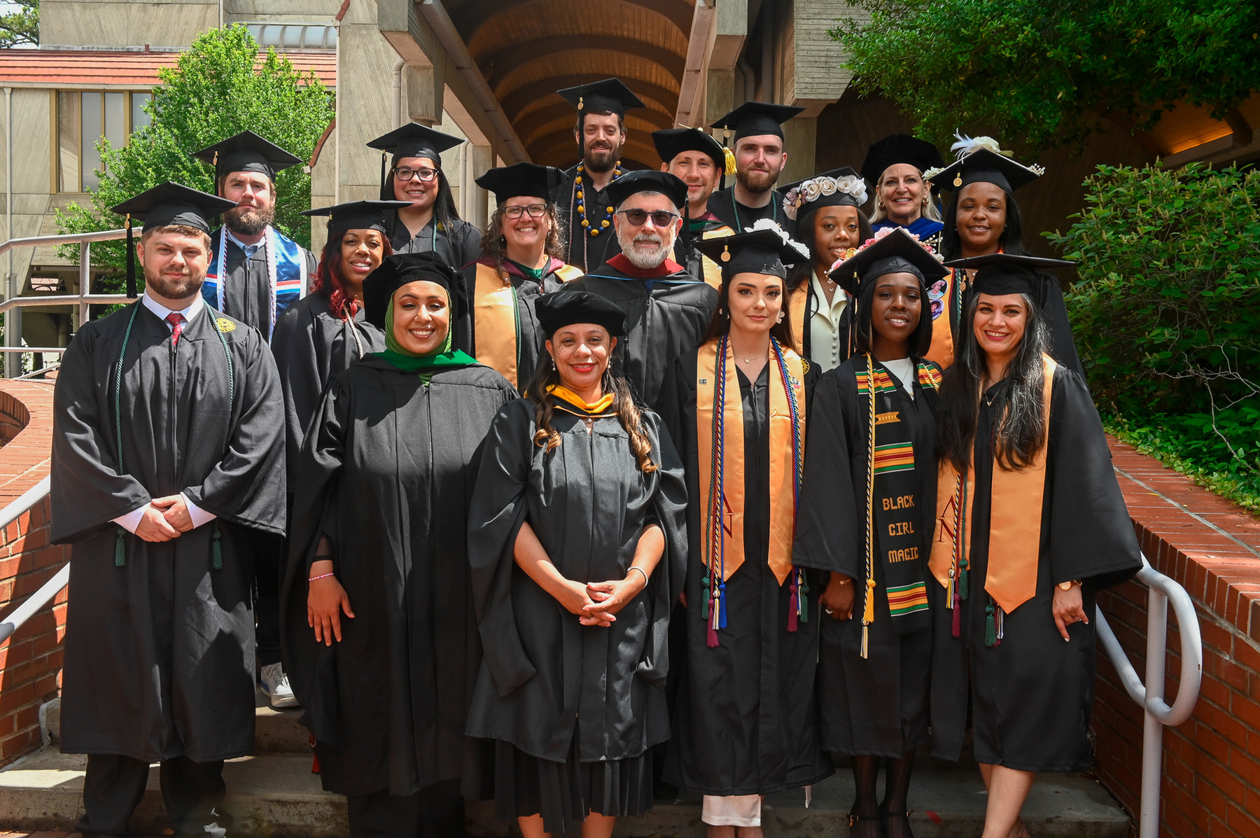 People wearing black graduation regalia standing in four rows and smiling