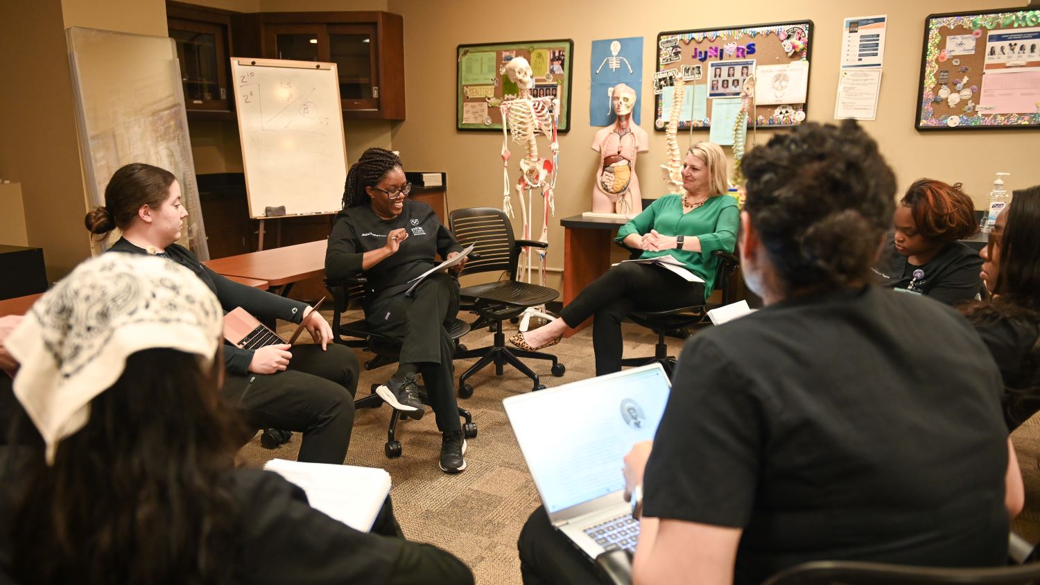 students sitting at desks in a circle with skeleton and anatomical model in background