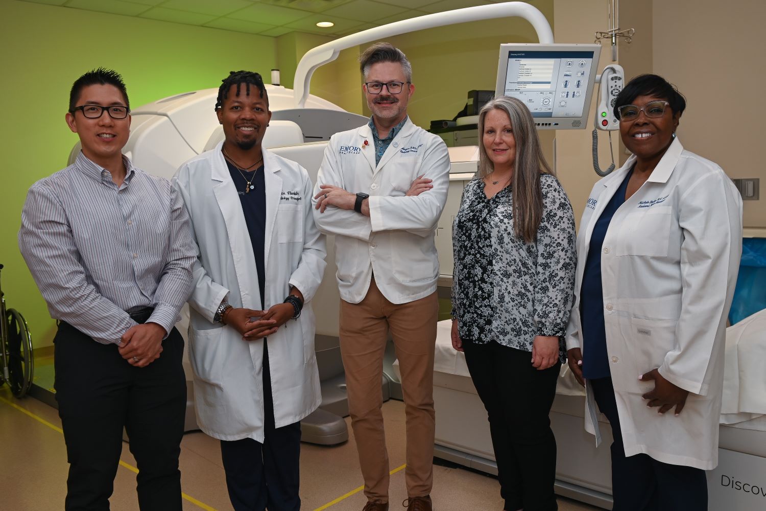 five people standing in front of ct imaging machine smiling