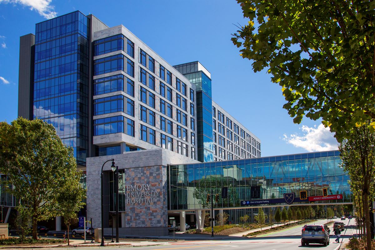 8 story building of glass and marble with bright blue sky and green trees