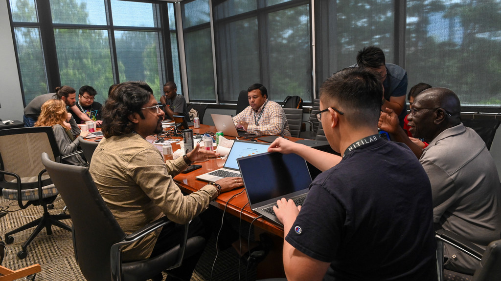 nine people around a large table talking and working on laptops