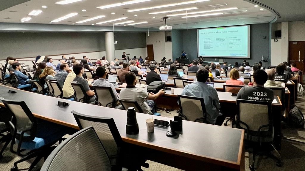 large lecture hall filled with people looking at presenter in front of a large screen