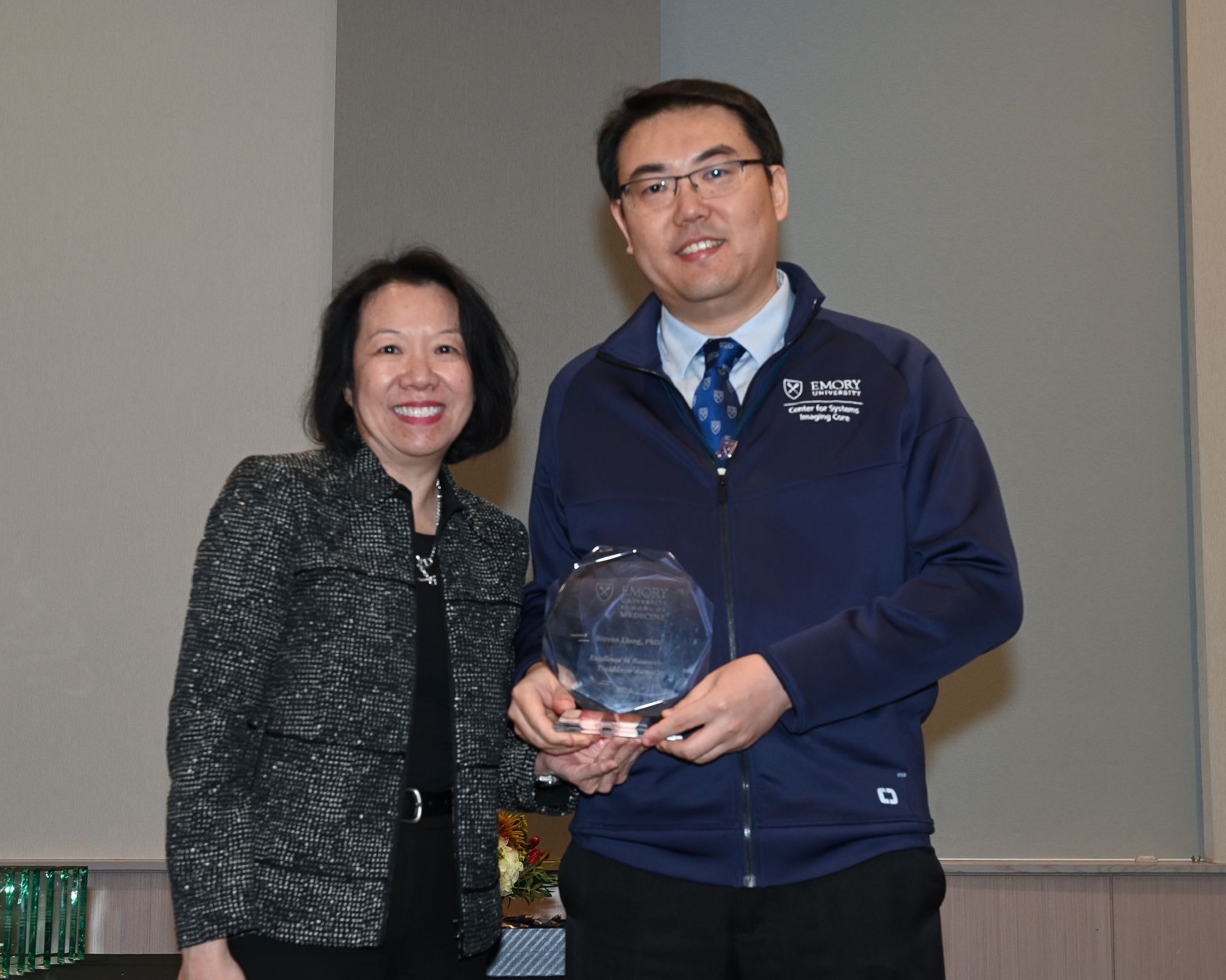 two smiling people holding a glass award and smiling at the camera