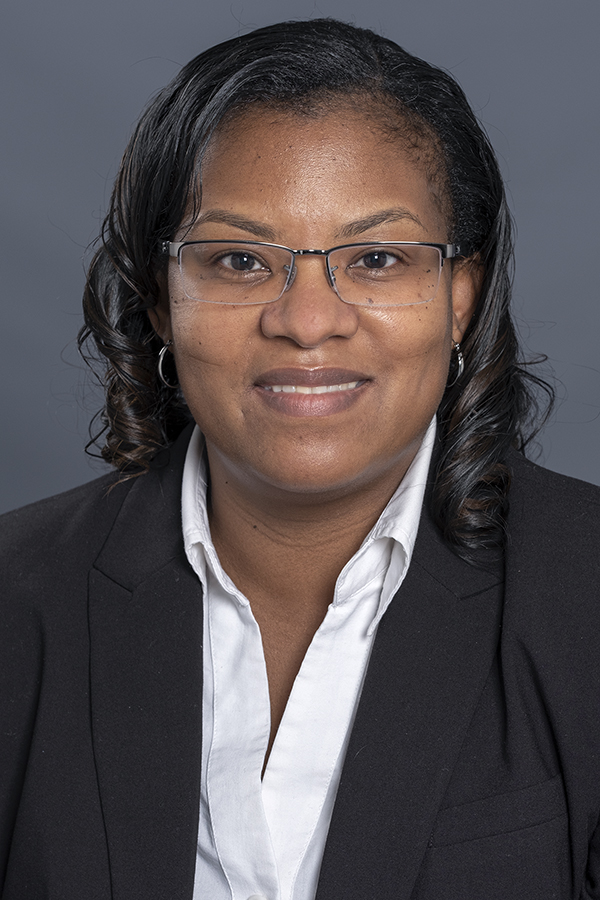 smiling woman with black hair and wearing glasses and a black jacket over a white button down shirt