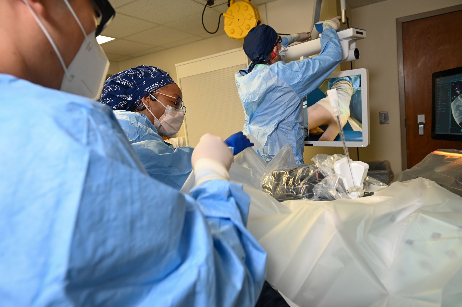 person adjusting computer cables while two other people work with an imaging robot attached to those cables