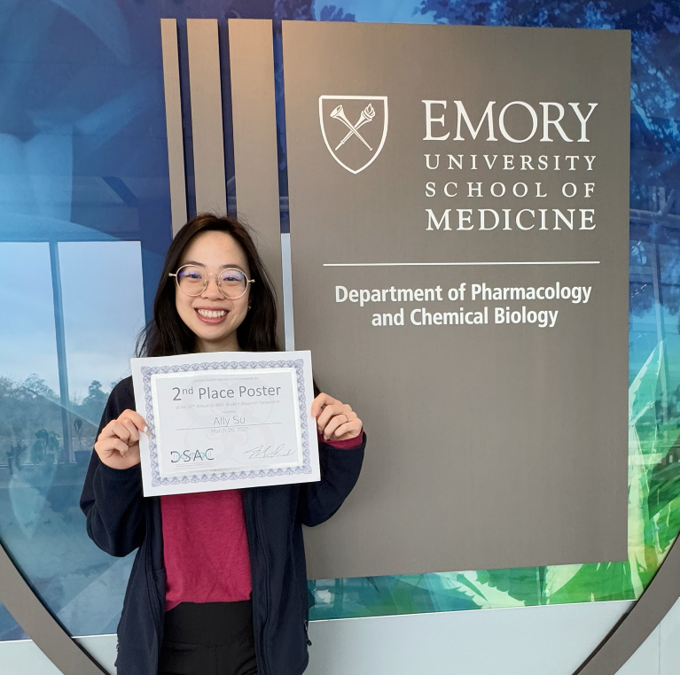 woman standing in front of poster presentation holding a paper award certificate