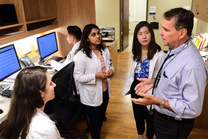 man talking with 3 women with white coats on in an office