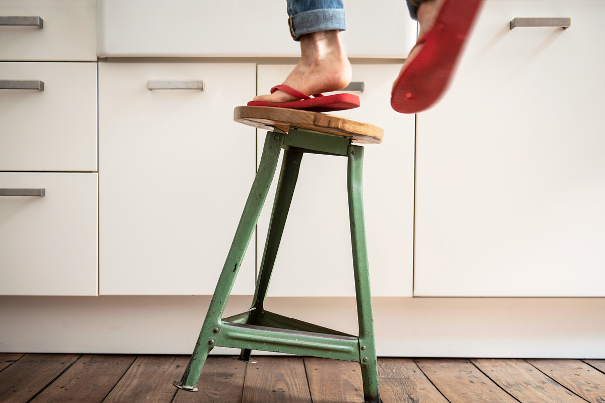 A tilting stool with unsteady feet earing red flip flops in front of cabinets