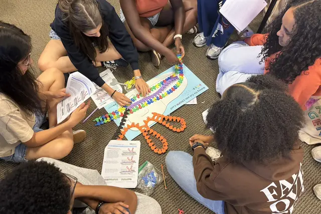 6 people sitting on the floor with handouts and colorful, plastic tracks