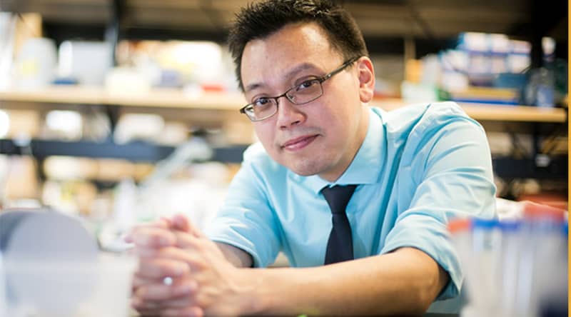 person with a tie and glasses leaning over a table with clasped hands