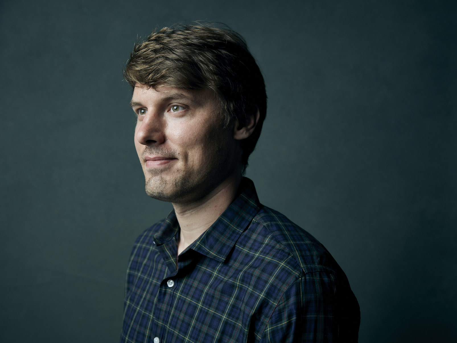 James Dahlman standing three-quarter profile, looking to the left against a blue-green background